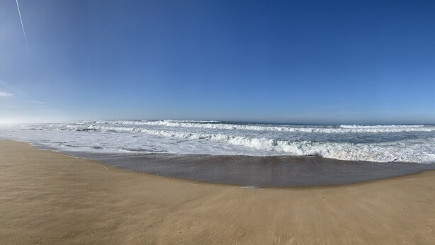Une vaste plage de sable fin, avec des vagues douces et un ciel bleu dégagé.