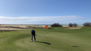 Un parcours de golf avec un mât de drapeau, un ciel dégagé et une vue lointaine sur la mer.