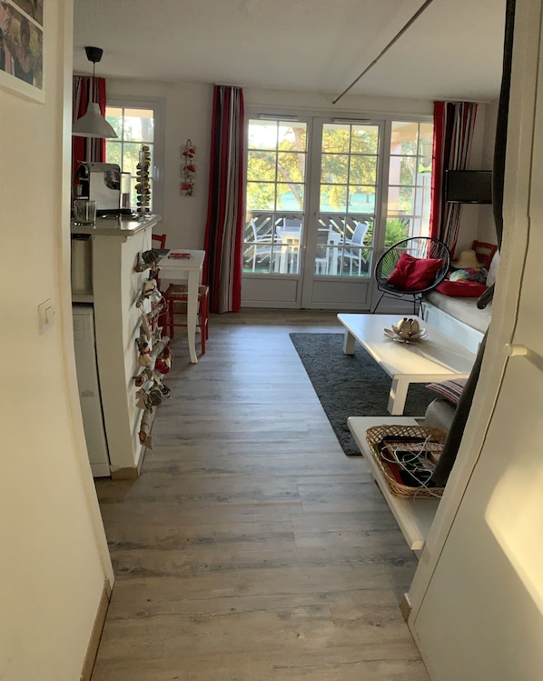 A narrow hallway with a kitchen area on one side, a dining area with a bench and chairs, and a seating area with a sofa and a TV.