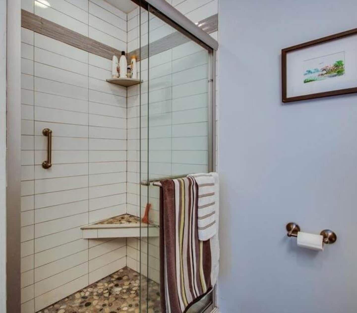 Un baño con cabina de ducha de vidrio, un perchero con una toalla a rayas y un cuadro en la pared.