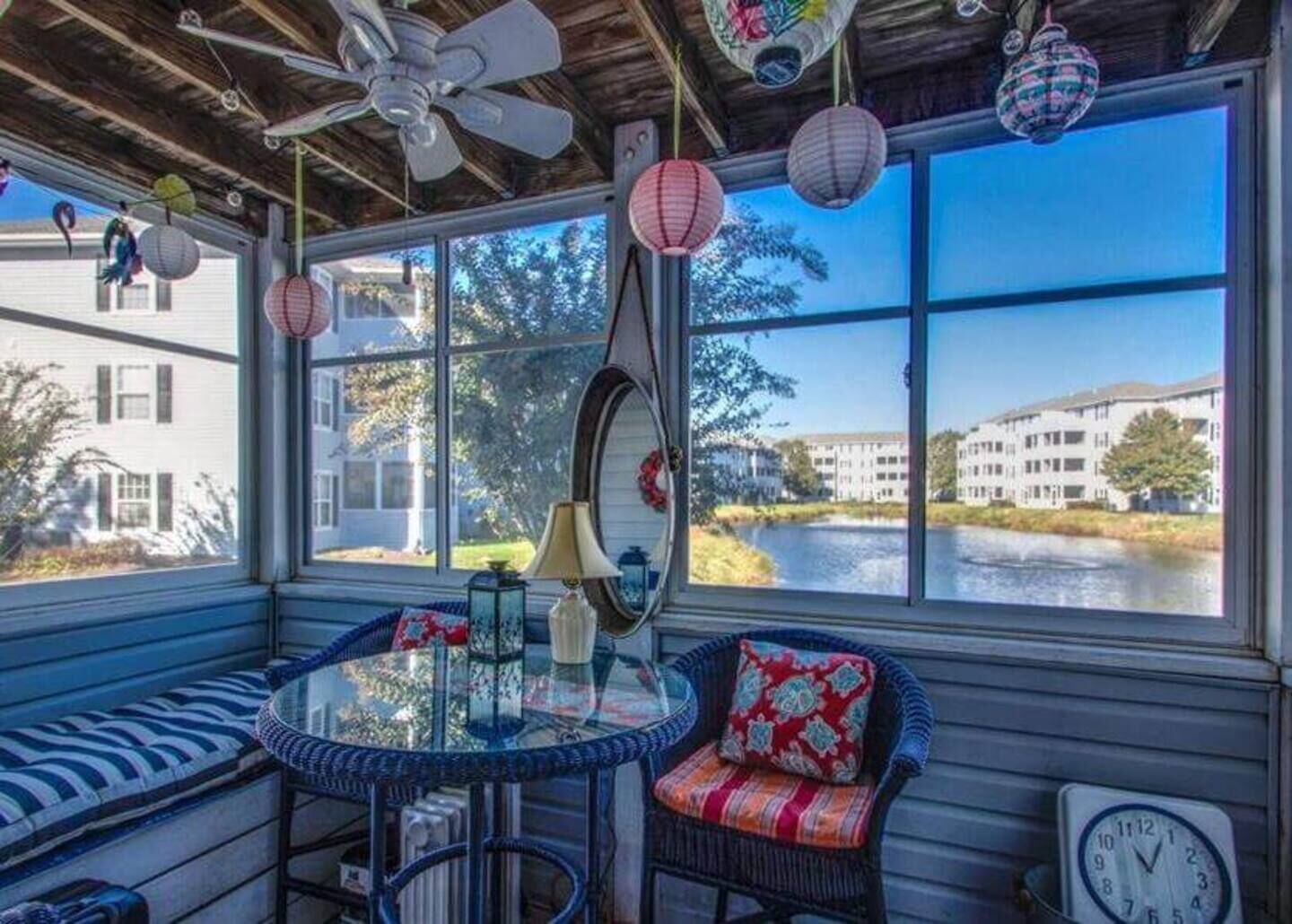 A sunroom with a view of a river, a ceiling fan, and a table with chairs.