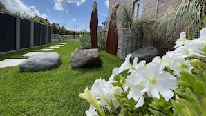 A well-maintained garden with a brick house, large rocks, and white flowers. - Strandvilla Wohnung Strand-lodge (Sylt)