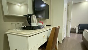 Ett litet, väl upplyst rum med ett vitt skrivbord, en tv som är monterad på väggen och en trästol.