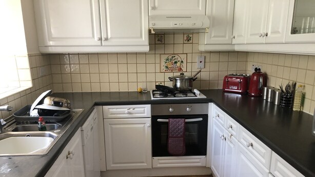 A kitchen with white cabinets, a black countertop, a stove, and a red toaster. - Nice 3-bed House in Farnham Royal Slough (Slough)
