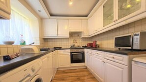 A kitchen with white cabinets, a washing machine, a microwave, and a wooden floor.