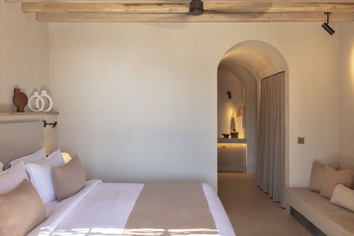 A bedroom with a large bed, a wooden ceiling, and a hallway leading to a bathroom.