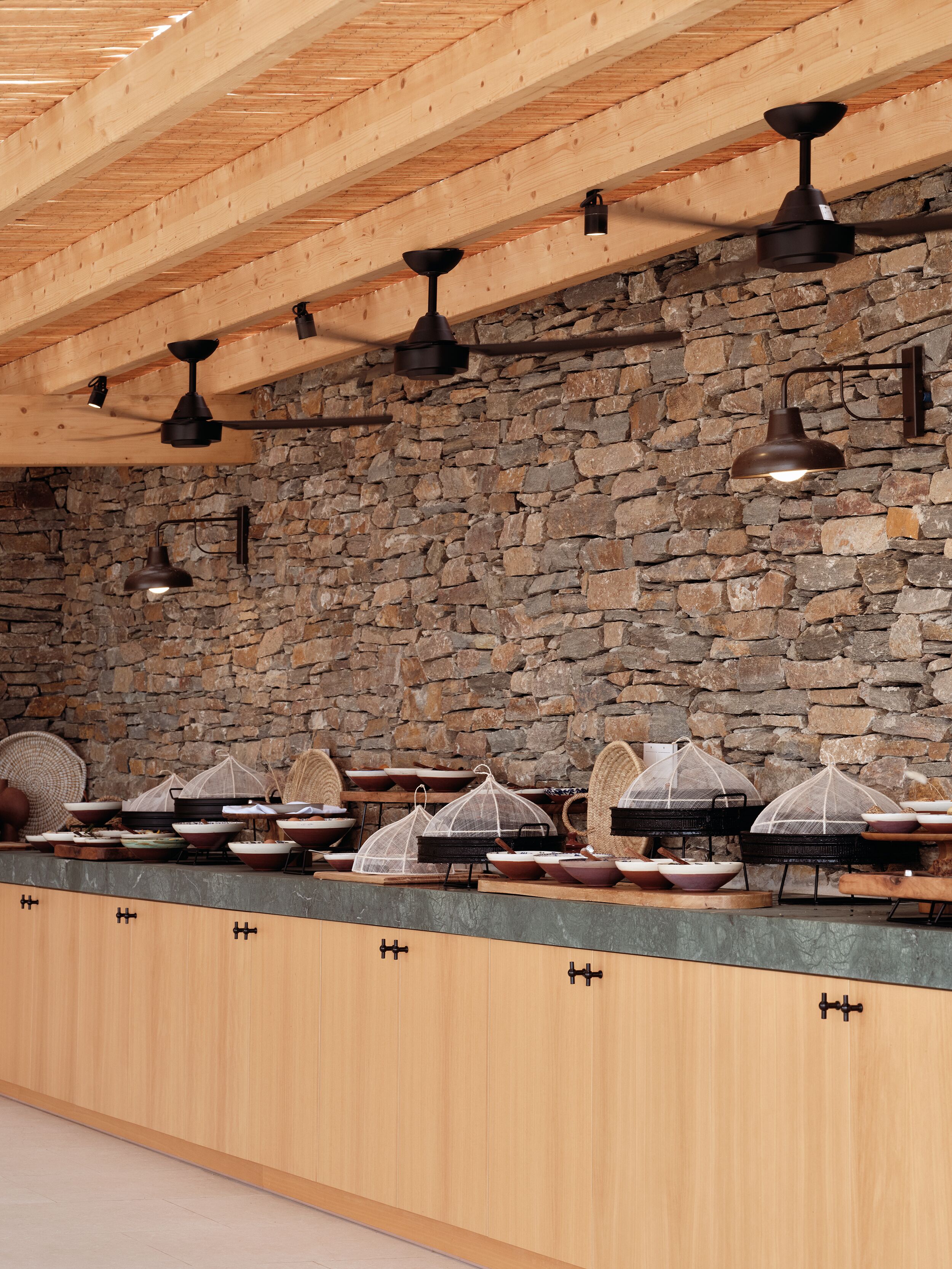 Una cocina con vigas de madera a la vista, paredes de piedra e iluminación moderna.