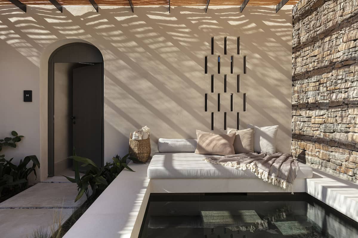 A modern interior with a stone wall, a sofa with cushions, a glass table, and a doorway.