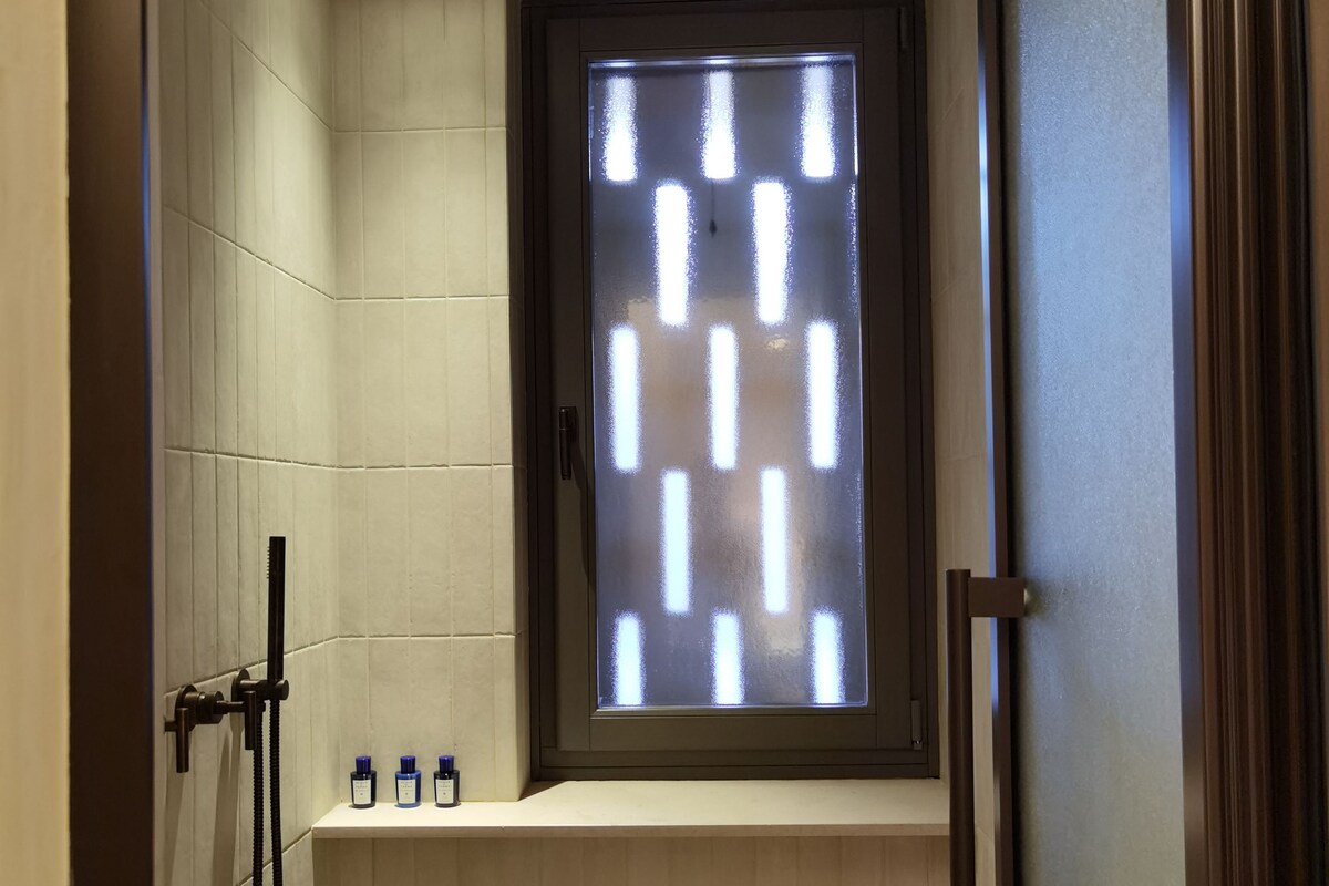 A small, modern bathroom with a bathtub, a shower, and a window with frosted glass.