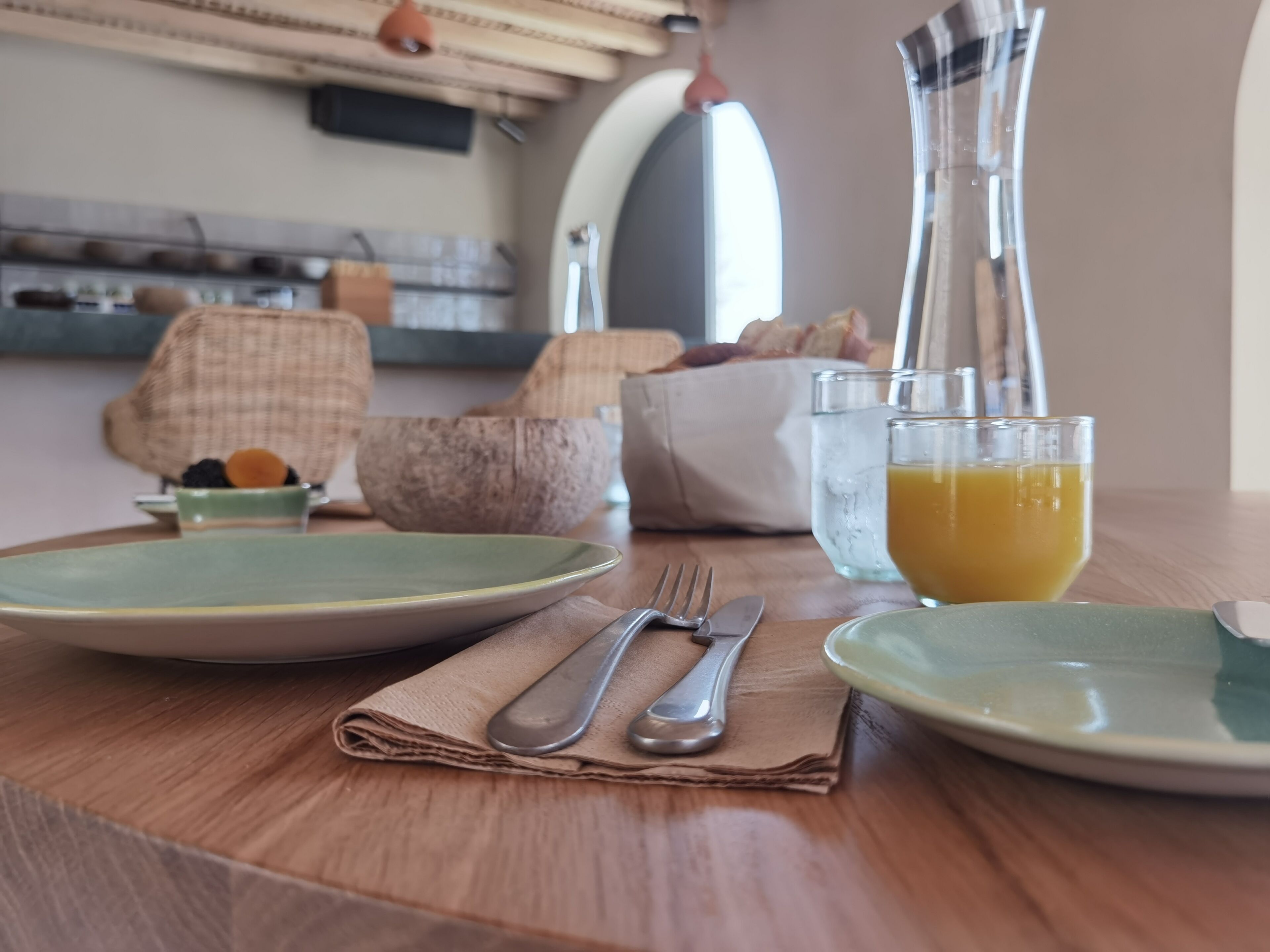 A breakfast setup with plates, cutlery, and a glass of orange juice on a wooden table.
