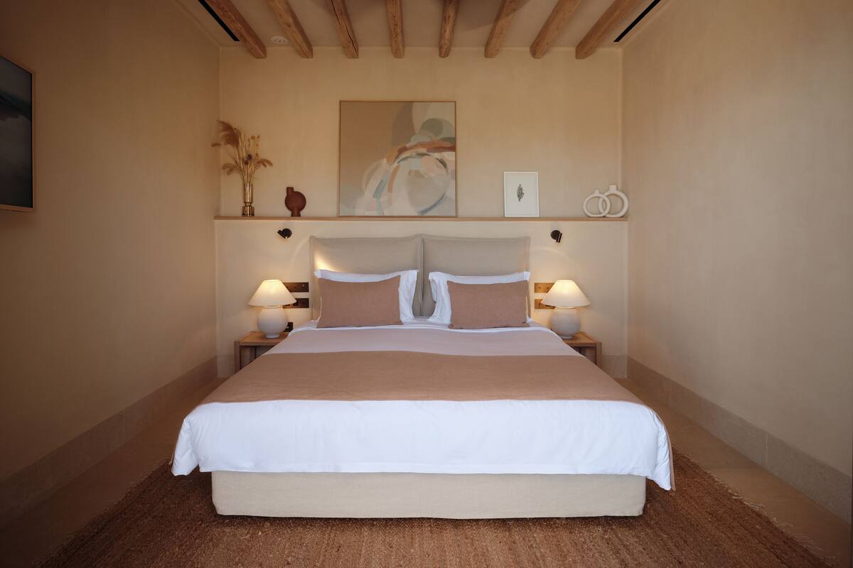 A bedroom with a large bed, wooden beams on the ceiling, and two bedside lamps.