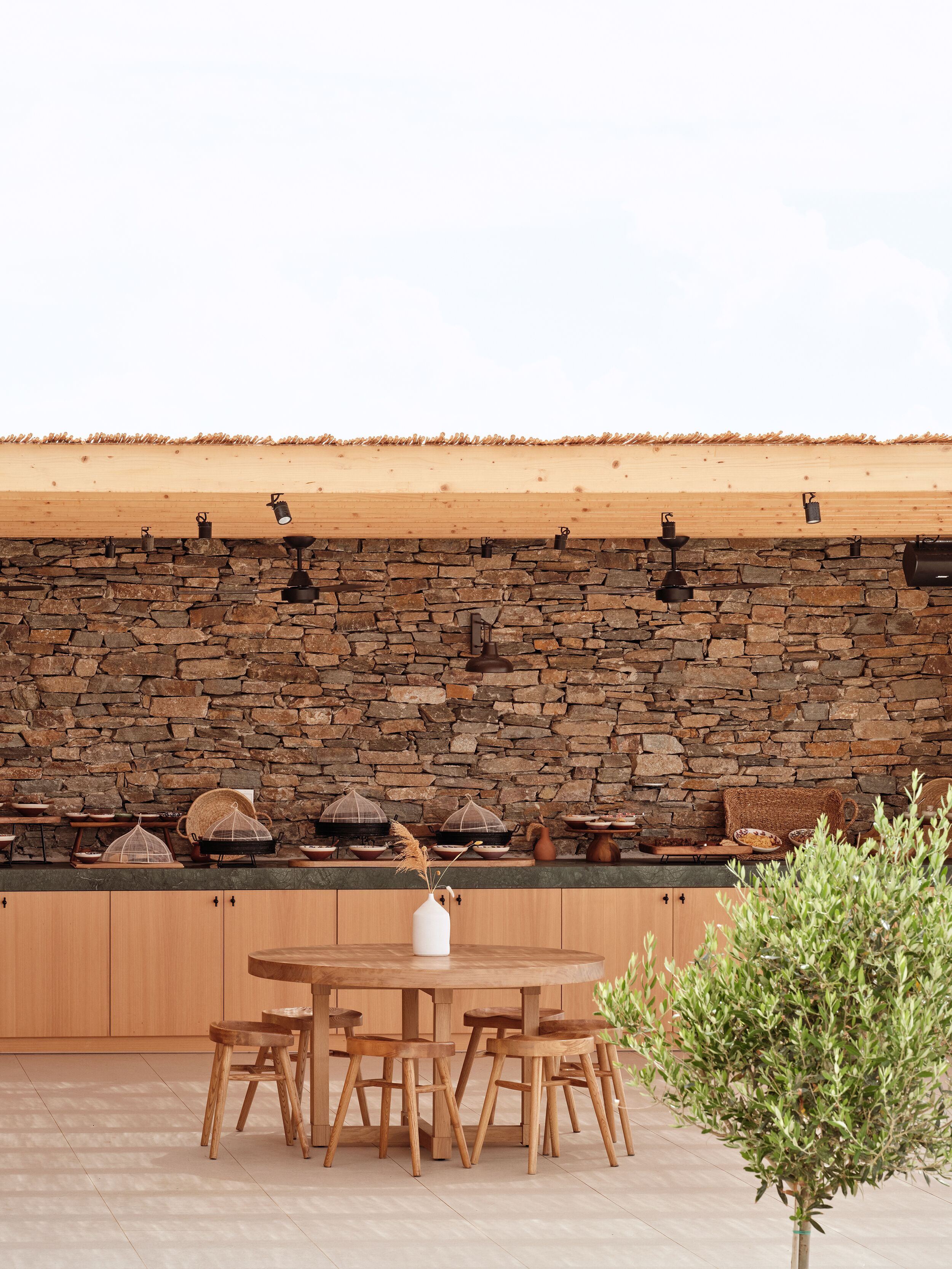 Un espacio de comedor al aire libre con pared de piedra, mesa y sillas de madera.