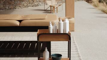 A modern outdoor seating area with a stone wall backdrop, a wooden bench with toiletries, and a lounge chair.