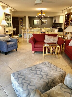 A living room with a red sofa, a blue patterned sofa, and a grey ottoman. There is a dining area in the background with white chairs and a table.