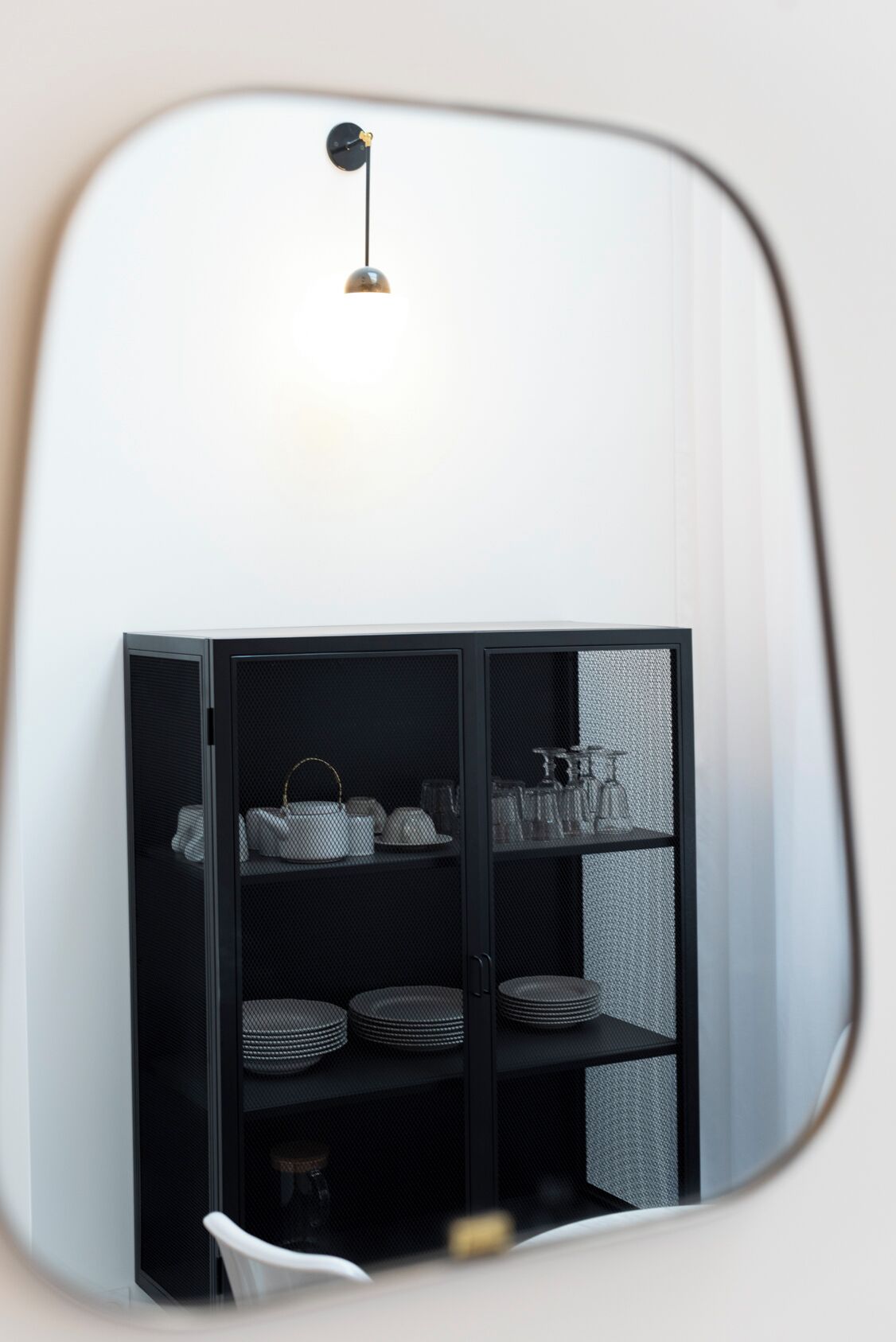 A mirror reflecting a black shelving unit with handbags and plates.