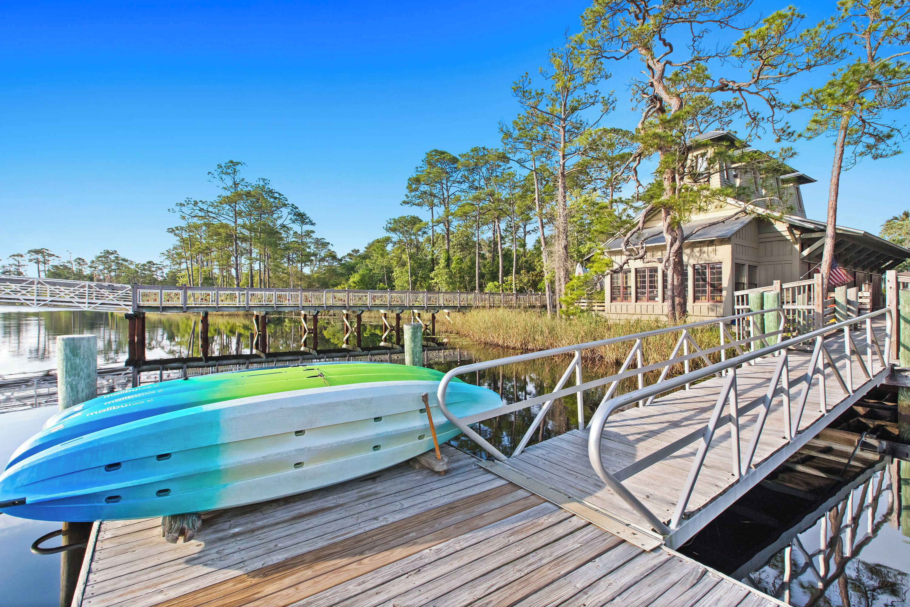 A wooden dock with a kayak, a wooden pier, and a house with a porch overlooking a body of water.