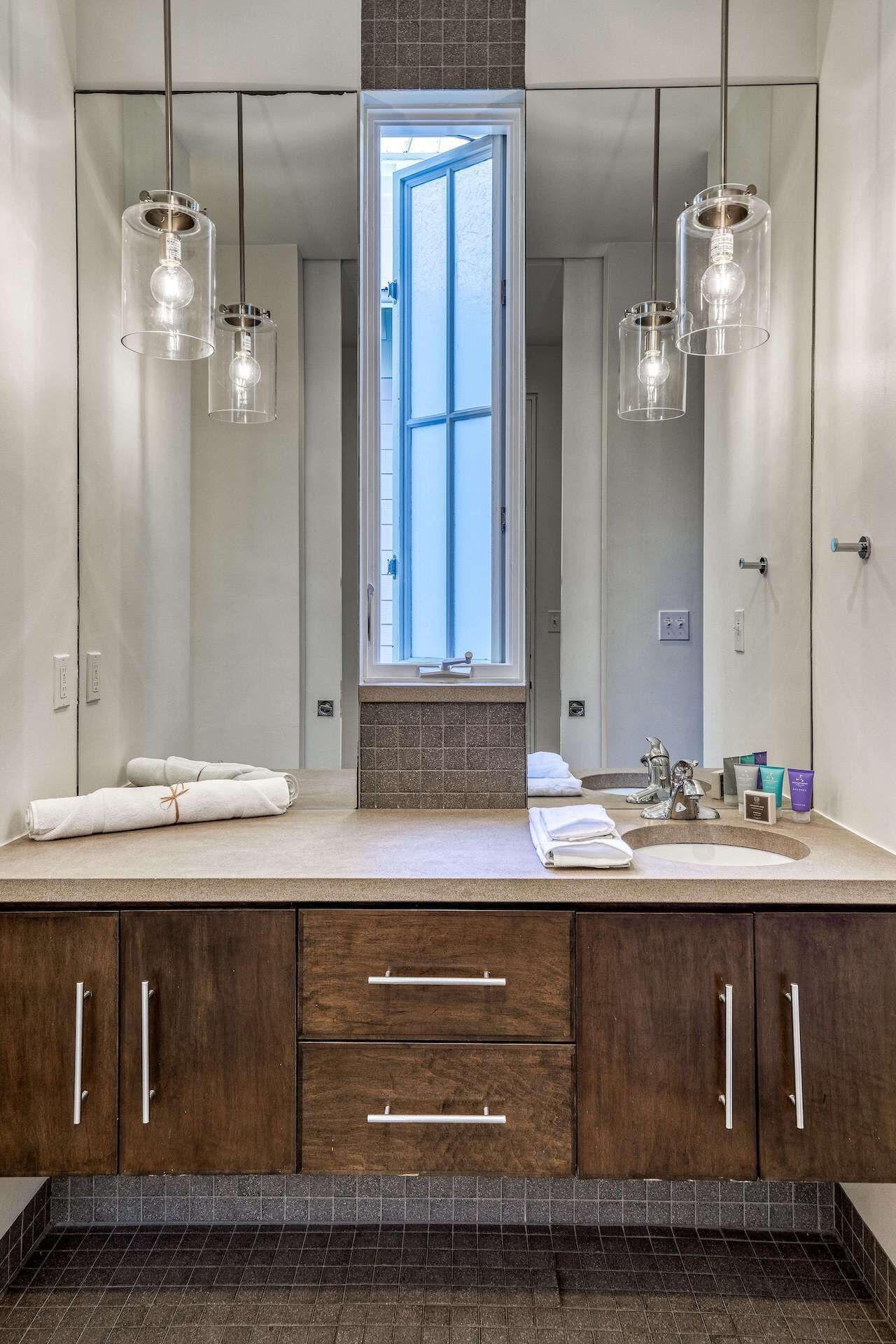 A modern bathroom with a large mirror, two sinks, and a window.