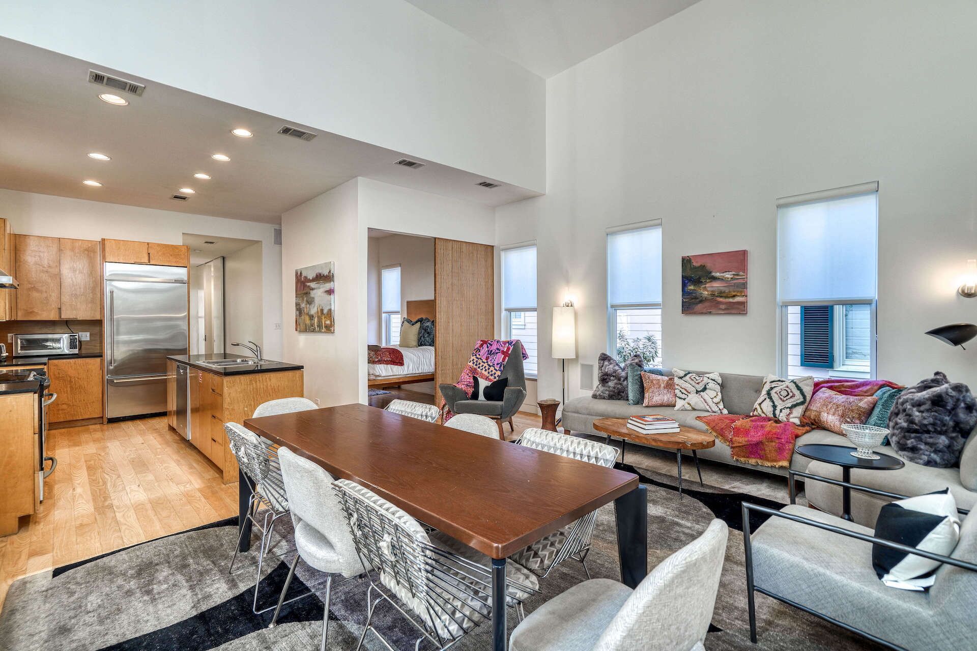 A spacious living area with a wooden dining table, comfortable seating, a kitchen with modern appliances, and large windows providing natural light.