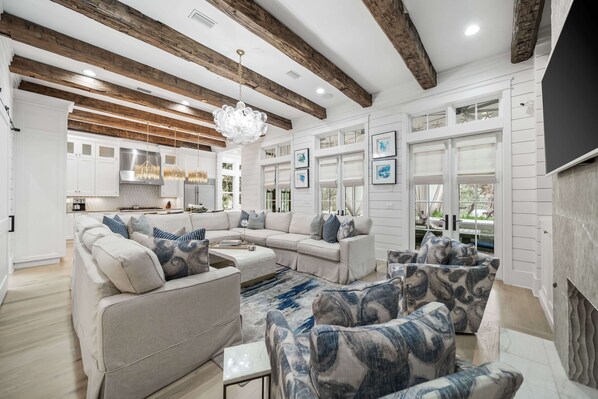 A spacious living room with a sectional sofa, patterned armchairs, a chandelier, and a fireplace.