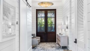 A hallway with a wooden door, a light-colored rug, and a small seating area with a lamp. - Amenity Loaded Designer Home on Western Lake with Pool, Elevator, Bikes, LSV (Santa Rosa Beach)