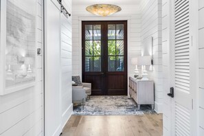 A hallway with a wooden door, a light-colored rug, and a small seating area with a lamp.