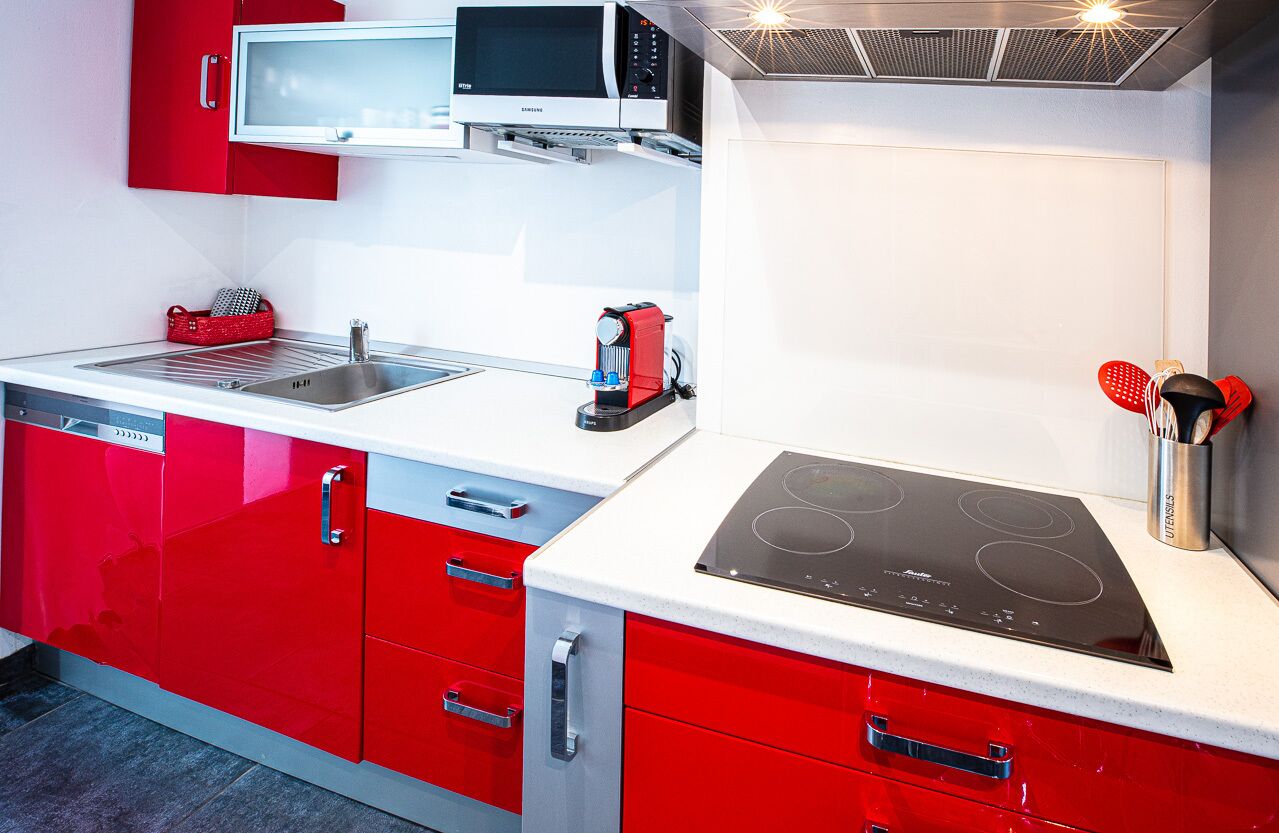 Une cuisine moderne avec des meubles de rangement rouges, un four à micro-ondes, une cuisinière et un lave-vaisselle.
