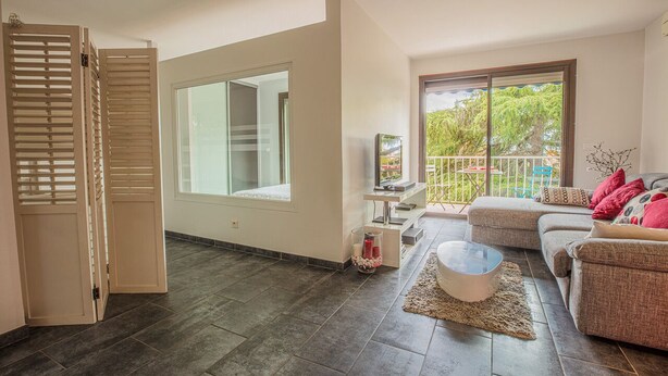 A spacious living room with a large sliding glass door leading to a balcony, a comfortable sofa set, a coffee table, and a television on a small table. - JUNGLE LUXURY FLAT WITH BALCONY AND PRIVATE PARKING IN CASSIS CENTER+WIFI (Cassis)