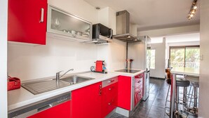 A modern kitchen with red cabinets, stainless steel appliances, and a bar area with stools. - JUNGLE LUXURY FLAT WITH BALCONY AND PRIVATE PARKING IN CASSIS CENTER+WIFI (Cassis)