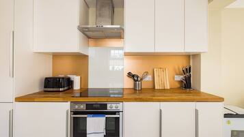 A compact kitchen with white cabinets, a wooden countertop, a toaster, a kettle, and a coffee maker.