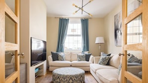 A living room with a sofa, ottoman, TV, and curtains. - Salisbury Residences by Charles Hope (Salisbury)