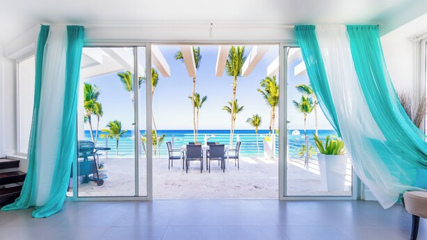 A room with a glass door leading to a beach view, featuring a table and chairs, and a potted plant. - Stunning Ocean View Condo in Punta Cana (Punta Cana)