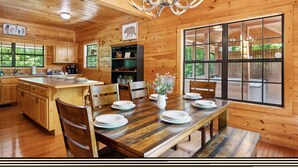 A wooden cabin interior with a dining area, kitchen, and large windows. - Kozy Bear 3 King BRs | Hot Tub | Pool Table (Sevierville)