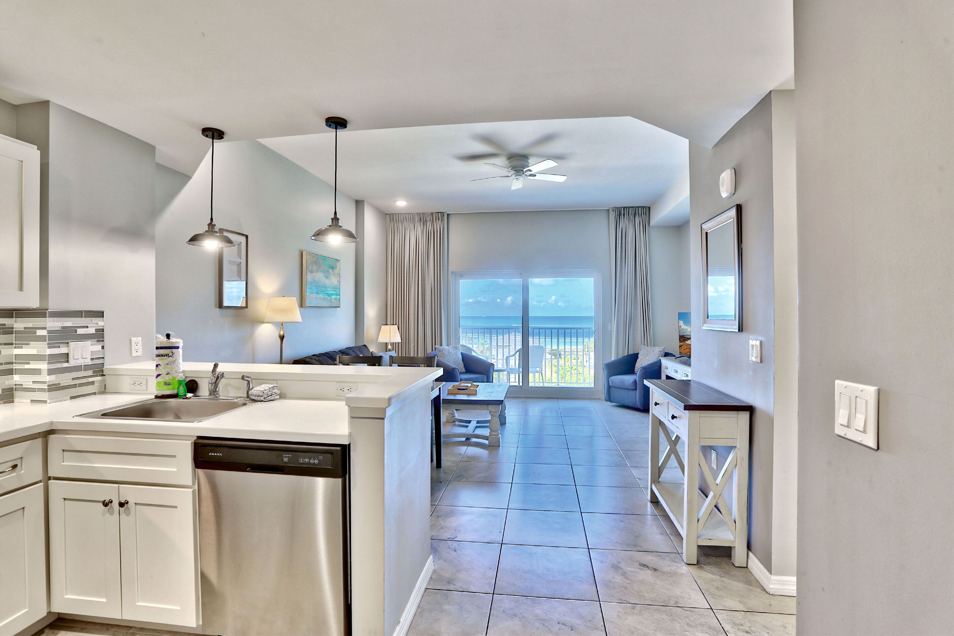 A modern kitchen with a dishwasher, a dining area with a table and chairs, and a view of the ocean through large windows.
