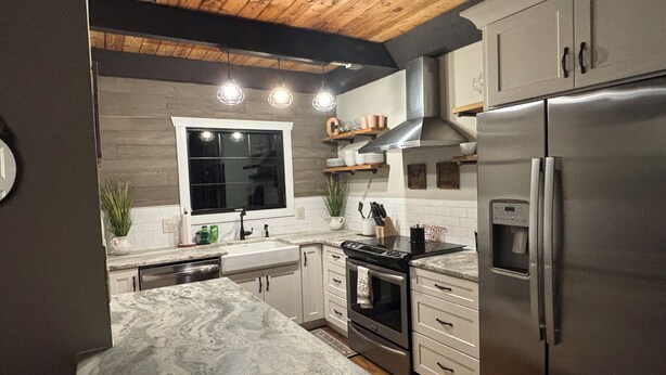 A modern kitchen with a marble countertop, stainless steel appliances, and wooden ceiling beams.