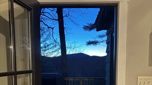 An open door leading to a wooden deck with a view of mountains and a parked vehicle.