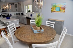 A modern kitchen with white cabinetry, a round wooden dining table, and a painting of a tropical scene.
