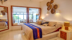 Ein Schlafzimmer mit Bett, Deckenventilator, großem Fenster und Blick ins Freie.