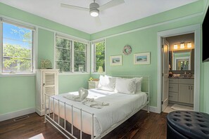 Een slaapkamer met een bed, een raam, een plafondventilator en een badkamer die door een open deur zichtbaar is.