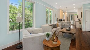 A spacious living room with a large window, a sofa, a coffee table, and a kitchen area in the background. - Sleepy Hollow Beach Resort, Cottage 9 – Family Fun on Lake Michigan! (South Haven)