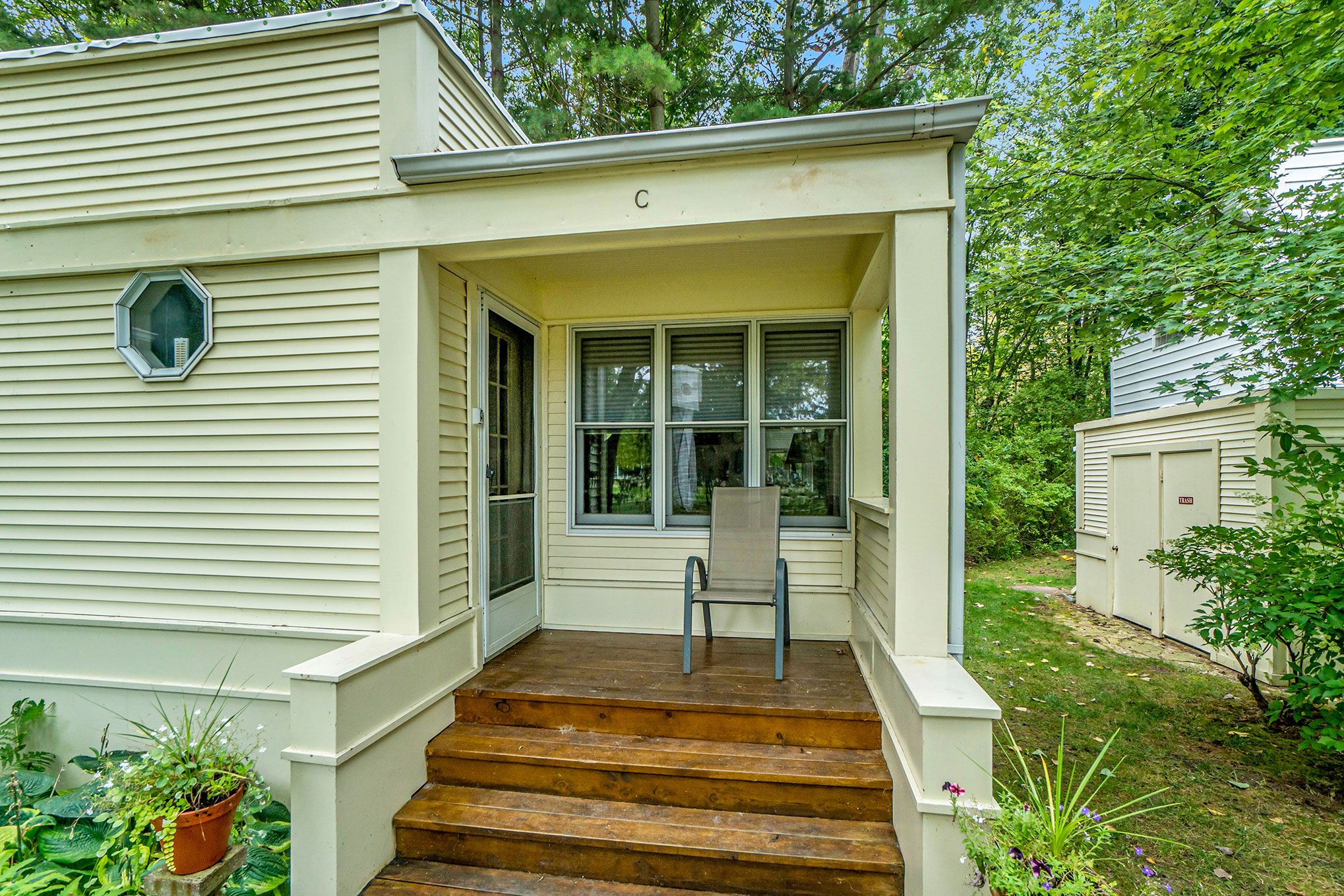 A single-story house with a front porch, a set of wooden steps leading to the entrance, and a chair placed on the porch.