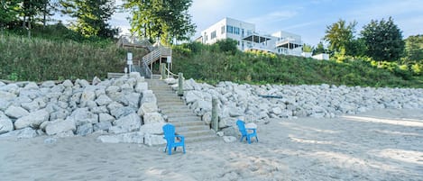 A beach with two blue chairs, a stone wall, and a staircase leading to a building.
