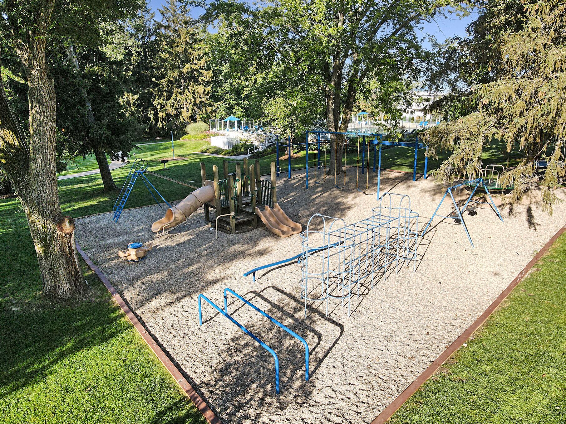 Un parque infantil con diversas estructuras de juego, como toboganes y columpios, rodeado de árboles y césped.