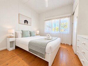 A bedroom with a bed, nightstands, a dresser, a window with curtains, and a wall-mounted artwork.