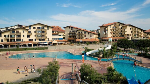 Un resort con varias piscinas, un tobogán acuático y una zona junto a la piscina con sombrillas.