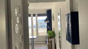 Un pasillo con un cartel que dice 'Bienvenue chez Nous', una puerta con diseños circulares, un comedor con mesa y sillas, y vista al exterior.