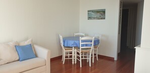 A dining area with a table and chairs, a sofa with a cushion, and a painting on the wall.