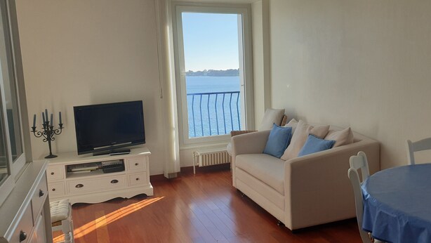 Ein Wohnzimmer mit einer Couch, einem Fernseher, einem Esstisch und Meerblick vom Balkon.