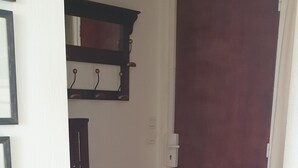 Ein Flur mit Holzboden, einer dunklen Holztür und einer weißen Wand mit Spiegel und Haken.