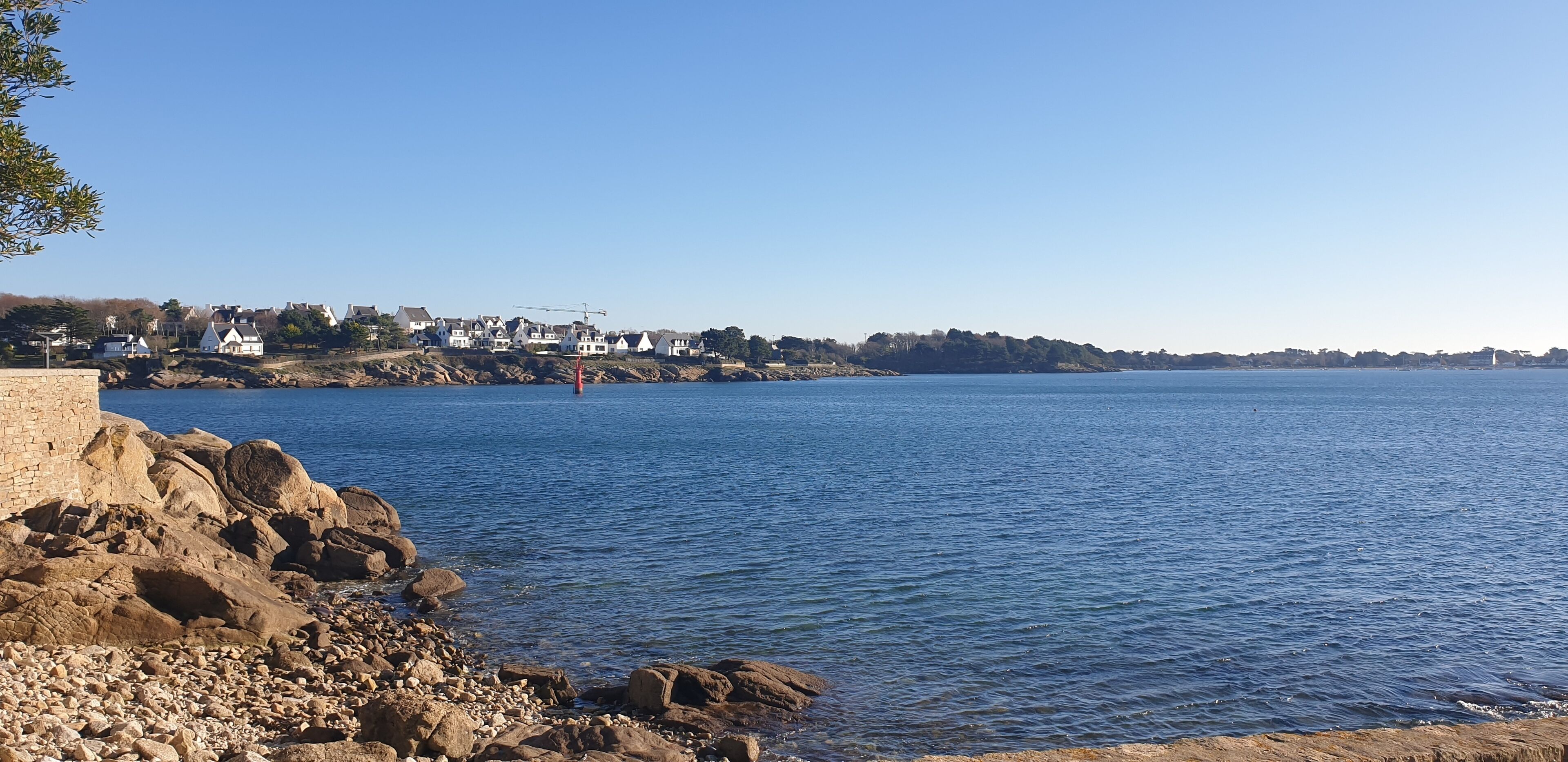A coastal town with a rocky shoreline, houses, and a clear blue sky.