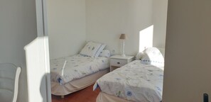 A bedroom with two single beds, a nightstand, a lamp, and a chair.